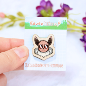 Pin de madera con diseño de la cara de Eevee, en su packaging.