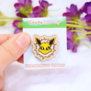 Pin de madera con diseño de la cara de Jolteon, en su packaging.