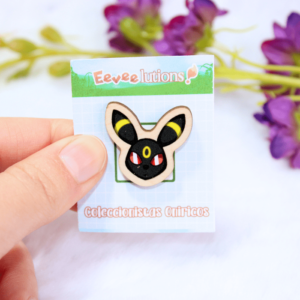 Pin de madera con diseño de la cara de Umbreon, en su packaging.