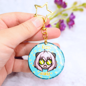 Llavero de resina con forma circular, con la cara de Anya y la frase "waku waku".