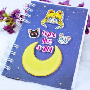 Cuaderno A6 con portada inspirada en Sailor Moon, Artemis y Luna. La portada tiene el diseño en relieve y la frase "Fight like a girl".
