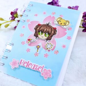 Cuaderno A6 inspirado en el anime Sakura Cazadora de Cartas. Portada con diseño de Sakura y Kero en relieve, con flores de cerezo y la palabra "Release!".