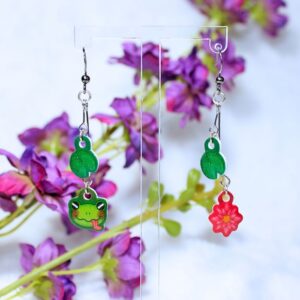 Pendientes de gancho de ranita con la lengua fuera, hojas de nenúfares y una flor.